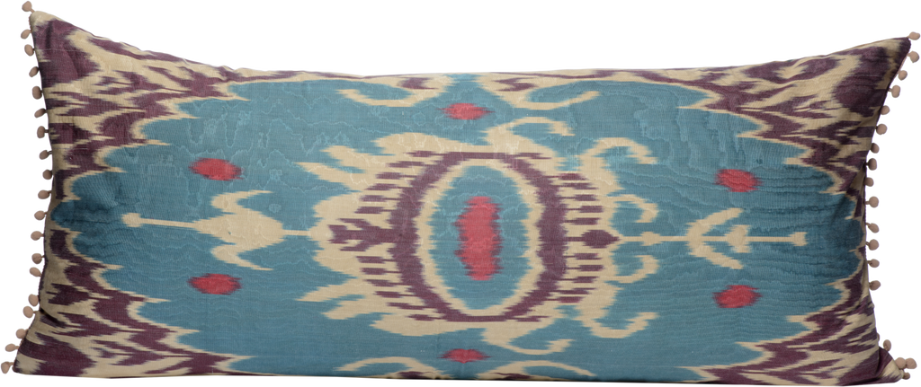 Front view of the hand woven reversible Silk Ikat bolster cushion with beautiful purple blue pattern on cream background with pompoms
